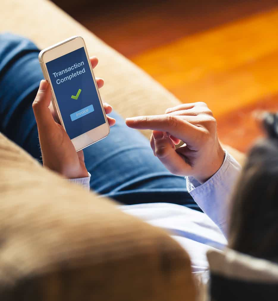 Lady on couch with iphone screen says transaction complete.