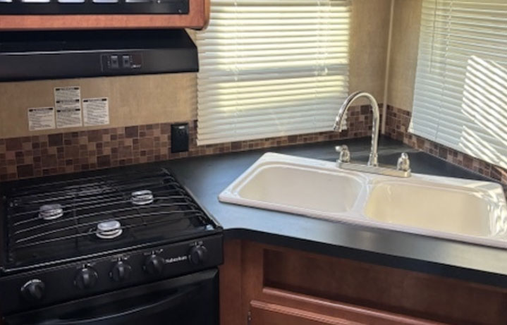 Image of kitchen sink with windows. Dark counter top with brown tile.